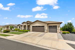 View of front of home featuring stucco siding, a garage, driveway, stone siding, and a front lawn