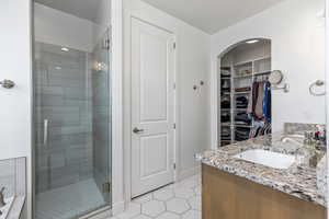 Bathroom featuring light tile patterned flooring, a spacious closet, double vanity, and a stall shower