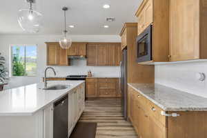 Kitchen with recessed lighting, decorative light fixtures, a kitchen island with sink, light wood-style floors, and brown cabinetry