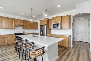 Kitchen with brown cabinetry, tasteful backsplash, pendant lighting, appliances with stainless steel finishes, and light wood finished floors