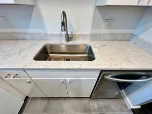 Kitchen view of the sink, light stone counters, and white cabinets