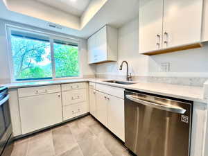 Kitchen with dishwasher, a sink, new cabinetry, light tile patterned floors, and cultured stone countertops