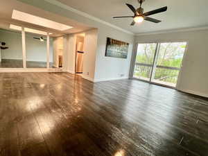 Unfurnished living room with ceiling fan, dark wood-style, low maintenence flooring, baseboards, and crown molding