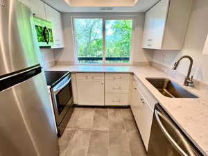 Kitchen with stainless steel appliances, a sink, light tile floors, white cabinetry, and a raised ceiling