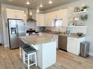 Kitchen featuring stainless steel appliances, wall chimney exhaust hood, light wood-style flooring, open shelves, and recessed lighting