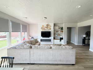 Living room with a textured ceiling, light wood-style floors, recessed lighting, and a glass covered fireplace