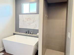 Bathroom featuring wood finished floors, a soaking tub, a tile shower, baseboards, and a textured ceiling