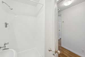 Full bath with a shower, wood finished floors, and baseboards