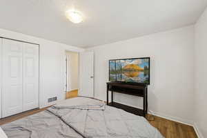 Bedroom featuring baseboards, wood finished floors, a closet, and a textured ceiling