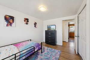 Bedroom with wood finished floors, a closet, baseboards, and a textured ceiling