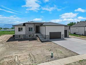 View of front facade with stone siding, an attached garage, concrete driveway, a mountain view, and stucco siding