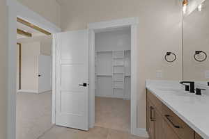 Bathroom with vanity, baseboards, a walk in closet, and tile patterned floors