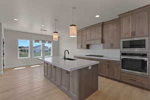 Kitchen featuring stainless steel appliances, a sink, light wood-style floors, light countertops, and a center island with sink