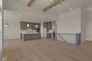 Unfurnished living room with beam ceiling, light wood-style floors, a sink, baseboards, and recessed lighting