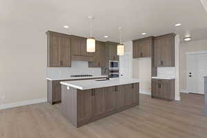 Kitchen featuring a sink, stainless steel appliances, baseboards, light wood finished floors, and recessed lighting