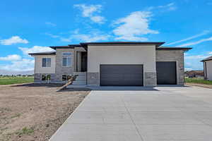 View of front facade with stone siding, driveway, a garage, and stucco siding
