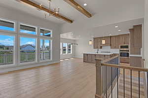 Kitchen featuring stainless steel appliances, open floor plan, beamed ceiling, light countertops, and light wood-type flooring