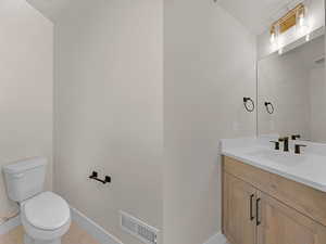 Half bath with vanity, tile patterned flooring, toilet, and baseboards