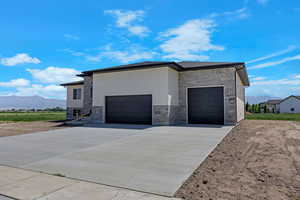 View of home's exterior with stone siding, a mountain view, driveway, a garage, and stucco siding