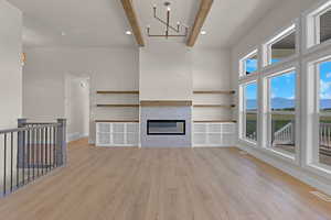 Unfurnished living room with beamed ceiling, light wood-type flooring, a chandelier, a glass covered fireplace, and a mountain view