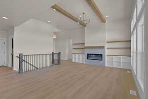 Unfurnished living room featuring light wood-type flooring, beamed ceiling, a chandelier, recessed lighting, and a glass covered fireplace