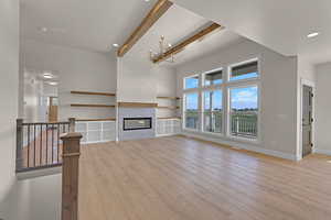 Unfurnished living room featuring beamed ceiling, light wood-style floors, baseboards, a glass covered fireplace, and recessed lighting