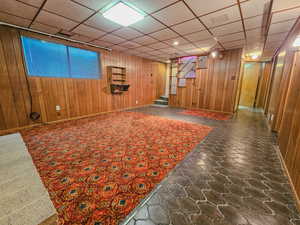 Finished below grade area featuring stairway, wooden walls, a paneled ceiling, stone finish flooring, and baseboards