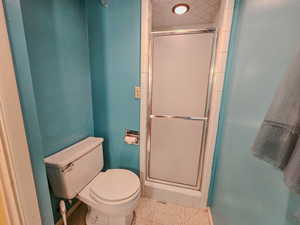 Bathroom featuring toilet, a shower stall, and baseboards