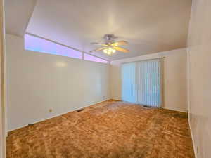 Carpeted empty room with a ceiling fan and vaulted ceiling