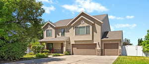 View of front facade featuring driveway, stucco siding, stone siding, and a garage