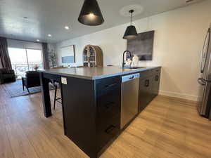 Kitchen featuring appliances with stainless steel finishes, a sink, open floor plan, light wood finished floors, and baseboards