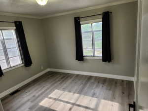 Unfurnished room with wood finished floors, ornamental molding, baseboards, and a textured ceiling