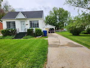 View of front of property with roof with shingles, an outdoor structure, a front lawn, and stucco siding
