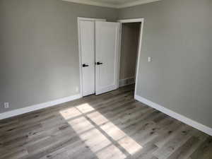 Unfurnished bedroom with crown molding, wood finished floors, and baseboards