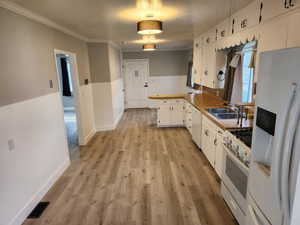 Kitchen featuring white appliances, a sink, white cabinets, a peninsula, and light wood-style floors