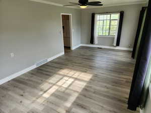 Spare room featuring crown molding, ceiling fan, baseboards, and wood finished floors