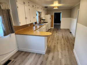 Kitchen with white appliances, light wood-style flooring, white cabinets, crown molding, and baseboards