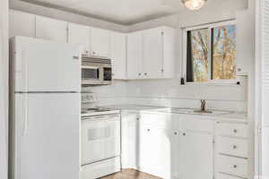 Kitchen with white appliances, light countertops, white cabinets, and a sink