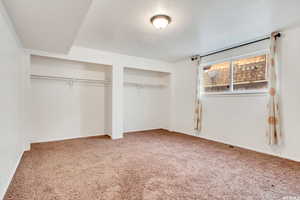 Unfurnished bedroom with carpet flooring, two closets, a textured ceiling, and baseboards