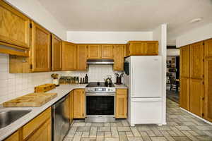 Kitchen featuring appliances with stainless steel finishes, under cabinet range hood, backsplash, light countertops, and brown cabinets