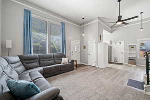 Living area featuring a towering ceiling, ceiling fan, baseboards, light wood-style flooring, and crown molding