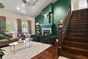 Living area with lofted ceiling, stairway, wood-type flooring, a glass covered fireplace, and ceiling fan