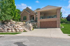 View of front of property featuring brick siding, an attached garage, driveway, a balcony, and stairs