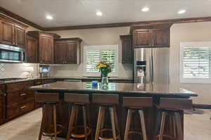 Kitchen with appliances with stainless steel finishes, a kitchen breakfast bar, dark brown cabinetry, dark stone countertops, and tasteful backsplash