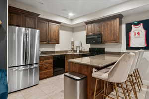 Kitchen with black appliances, a peninsula, a sink, dark stone countertops, and a breakfast bar