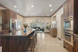 Kitchen with appliances with stainless steel finishes, open floor plan, crown molding, a chandelier, and dark stone countertops