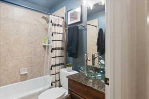 Bathroom featuring vanity, shower / tub combo with curtain, and toilet