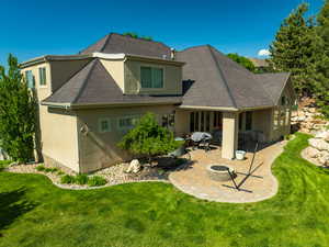 Rear view of property featuring stucco siding, a patio area, a fire pit, and a yard