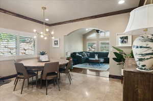 Dining room with crown molding, arched walkways, a chandelier, baseboards, and ceiling fan