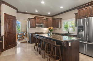 Kitchen featuring stainless steel appliances, a sink, crown molding, a breakfast bar area, and arched walkways